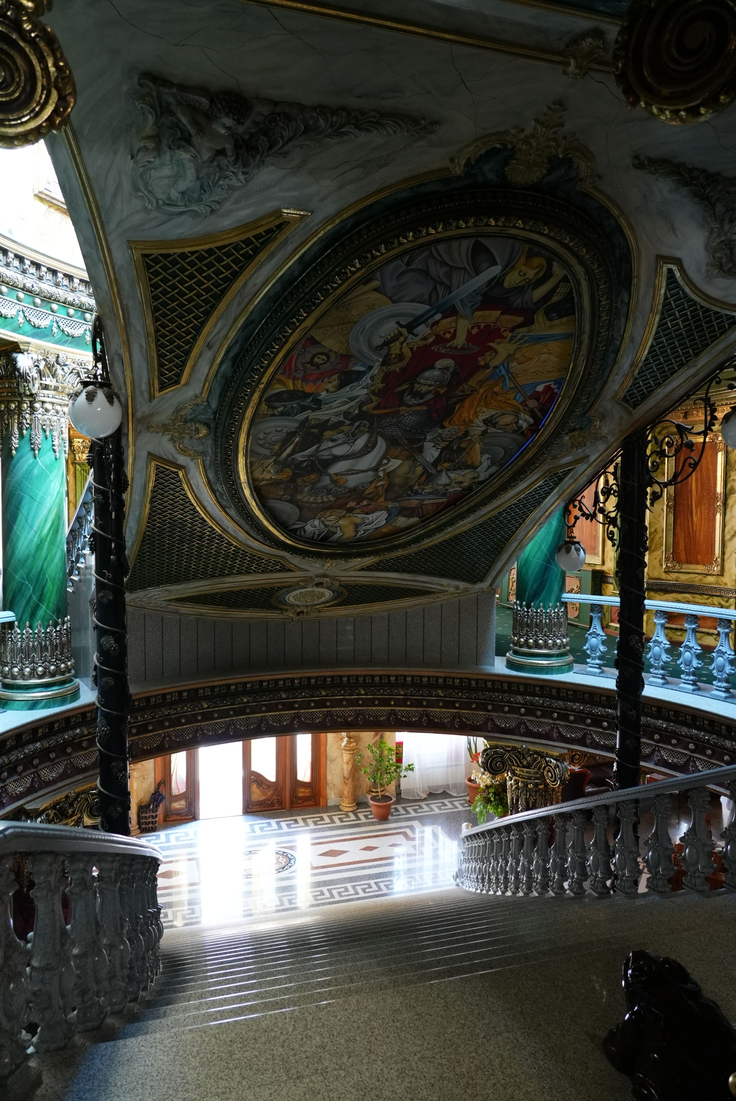 Interior ornamentado com um detalhado mural no teto, uma escadaria imponente e elementos arquitetônicos clássicos.