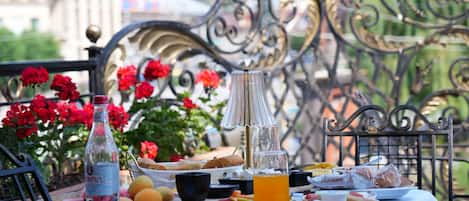 An outdoor dining table with a variety of food items and drinks, surrounded by metal chairs and a decorative metal fence.