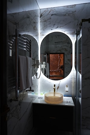 A modern bathroom with a marble wall, a round mirror, a towel rack, and a sink with a gold faucet. - Alexandrapol Hotel Palace (Gyumri)