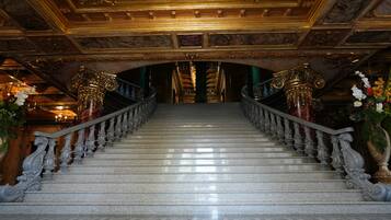 Una gran escalera con balaustradas ornamentales y un candelabro, que conduce a una habitación oscura con un techo alto.