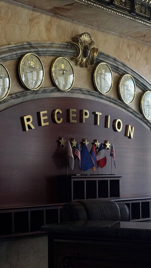 A reception area with a marble wall, multiple clocks, and flags. - Alexandrapol Hotel Palace (Gyumri)