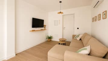 Una sala de estar moderna con un sofá, una televisión, una mesita y una planta en maceta.