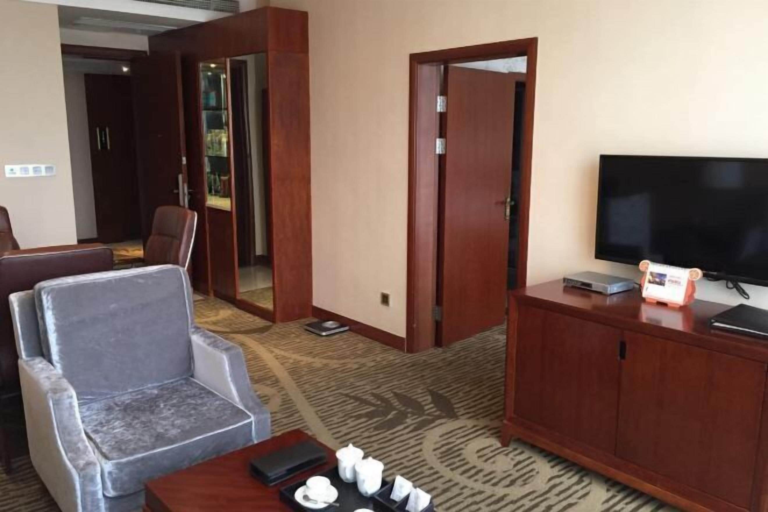 A hotel room with a seating area, a television, and a cabinet.