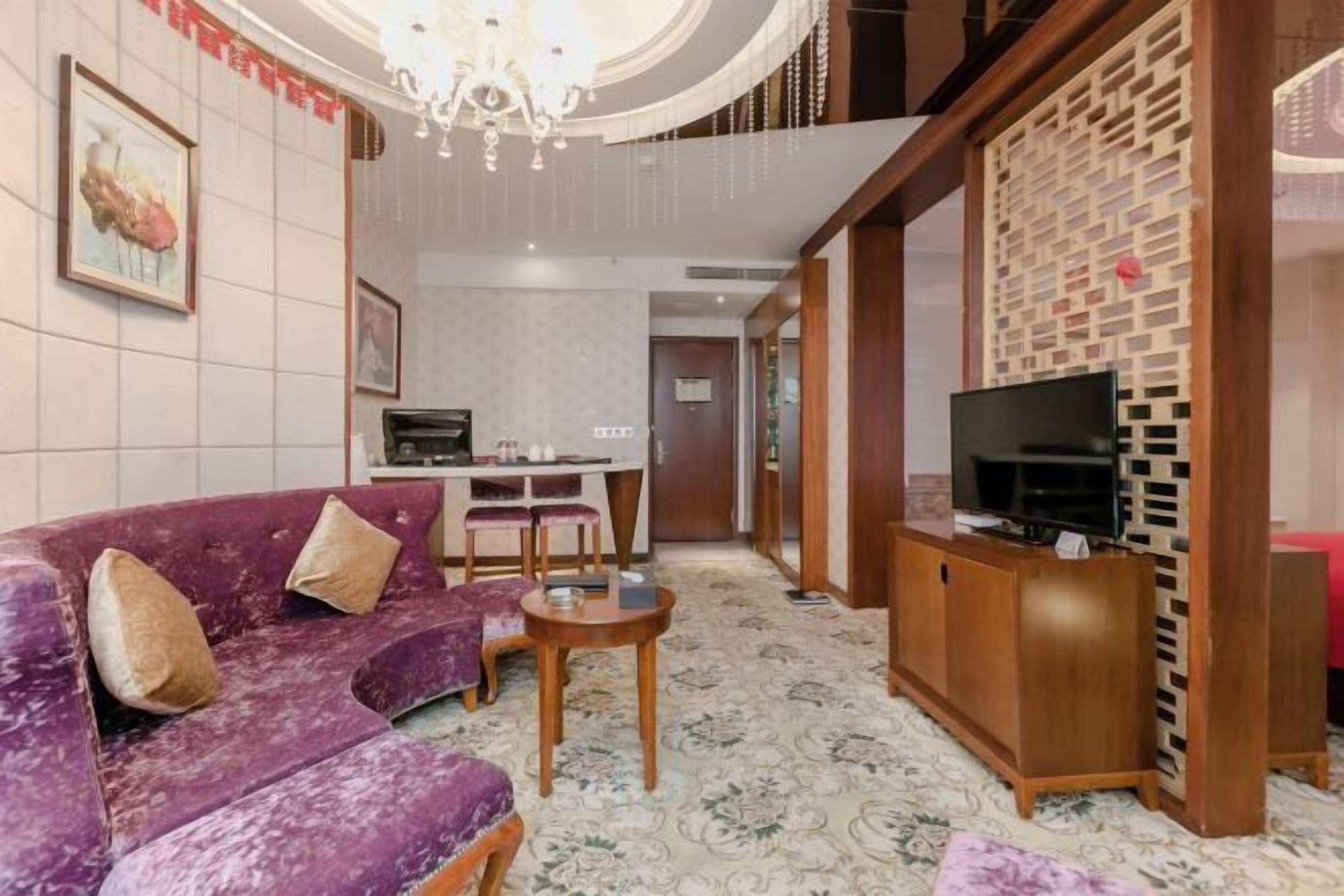 A living room with a purple sofa, a small table, a TV on a wooden stand, and a decorative wall.