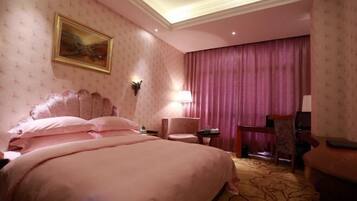 A hotel room with a large bed, a desk, a chair, and a painting on the wall.