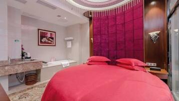 A hotel room with a large bed, a vanity with a mirror, and a red accent wall.