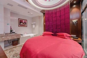 Quarto de hotel com uma cama grande, uma penteadeira com espelho e uma parede em destaque vermelha.