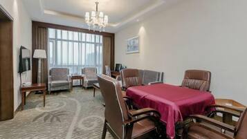A hotel room with a dining table, chairs, a chandelier, a TV, and a large window.