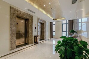 Un moderno vestíbulo de hotel con paredes de mármol, ascensores y una gran planta en maceta.
