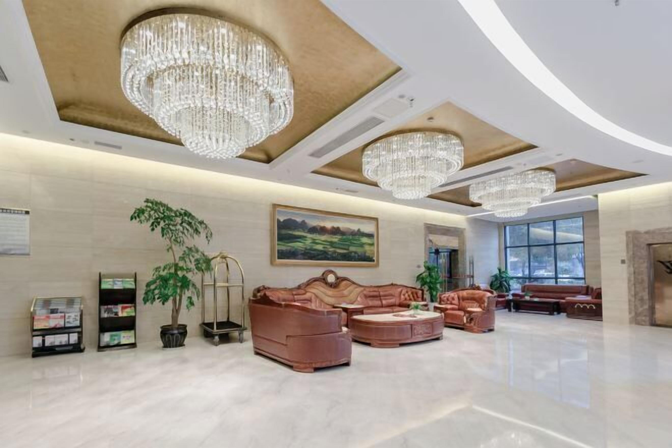 A spacious lobby with a high ceiling, chandeliers, leather sofas, and a large window.