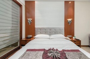 Habitación de hotel con una cama grande, dos mesitas de noche y una ventana con persianas.