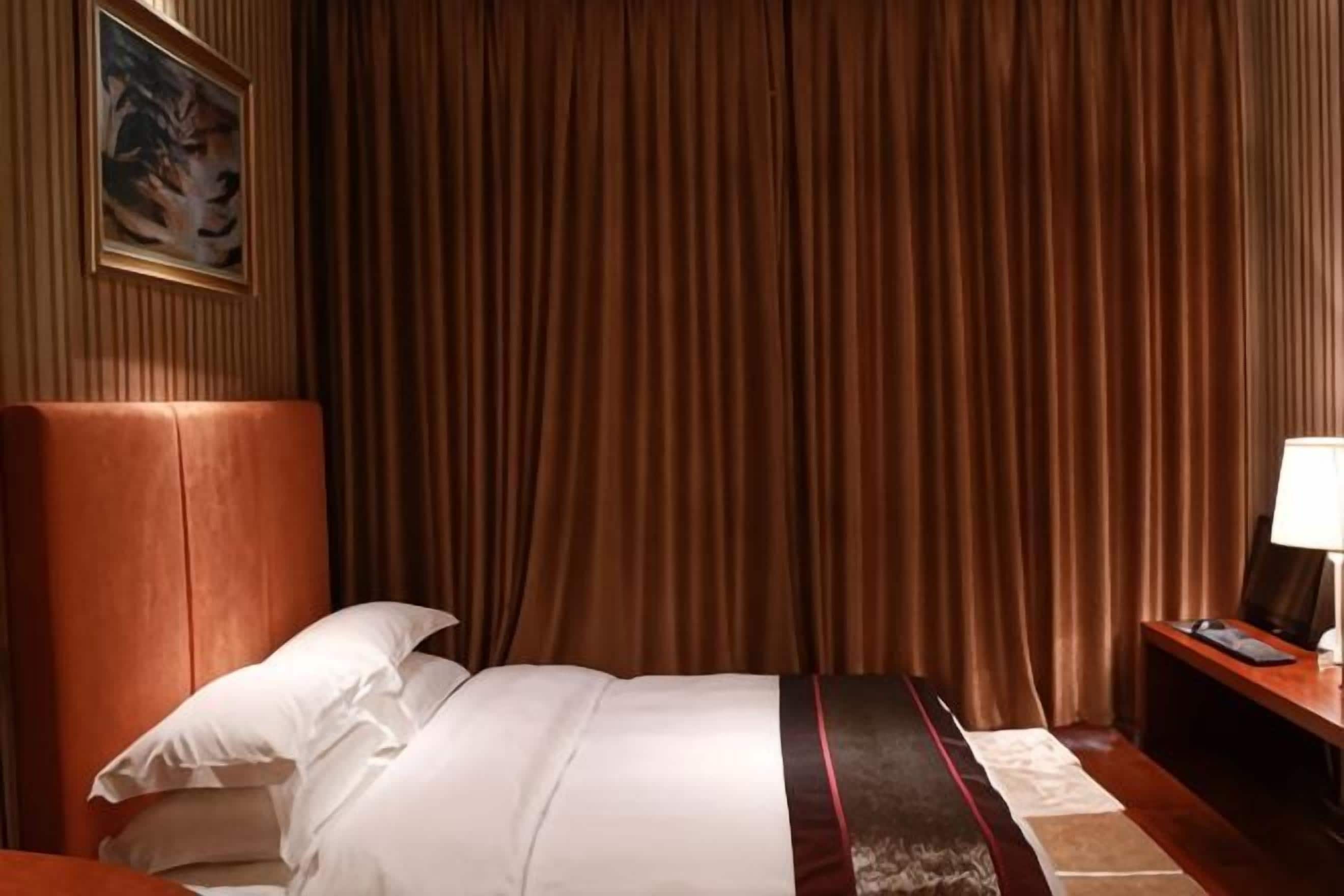 A hotel room with a large bed, a headboard, a nightstand, and a curtain.