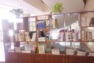 Una biblioteca con varias estanterías llenas de libros, una planta en maceta en la estantería superior y una vitrina de cristal en la parte frontal.