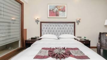 A hotel room with a large bed, two bedside tables, a nightstand, a chair, and a painting on the wall.