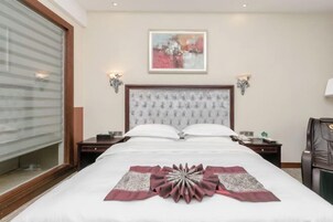 Quarto de hotel com uma cama grande, duas mesas de cabeceira, um criado-mudo, uma cadeira e um quadro na parede.