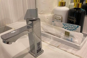 Une salle de bain avec un robinet moderne, un flacon de gel douche et un flacon de shampoing.