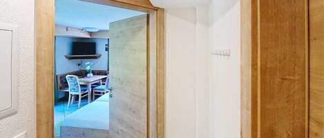 Un pasillo que conduce a un comedor con una mesa y sillas, un televisor montado en la pared y una puerta de madera.