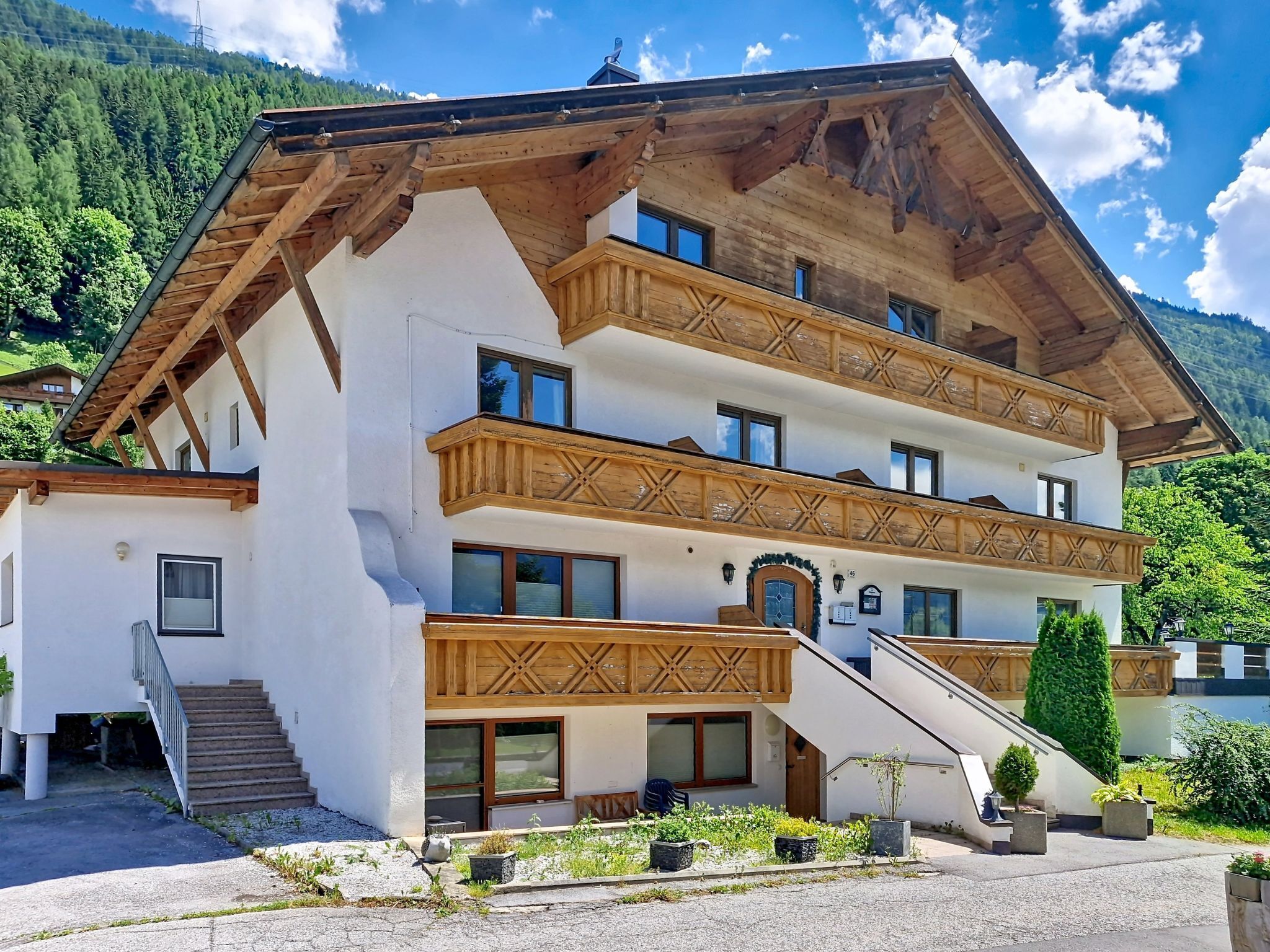 Un immeuble à plusieurs étages doté de balcons en bois, d’un escalier et offrant une vue sur un paysage montagneux.