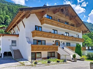 Un edificio de varios pisos con balcones de madera, una escalera y vistas a un paisaje montañoso.