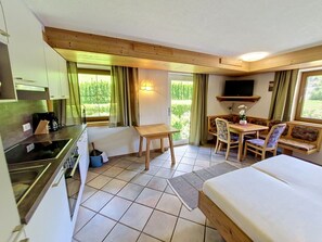 Ein kompakter Raum mit Küchenzeile, einem Esstisch mit Stühlen, einer Couch und einem an der Wand befestigten Fernseher.