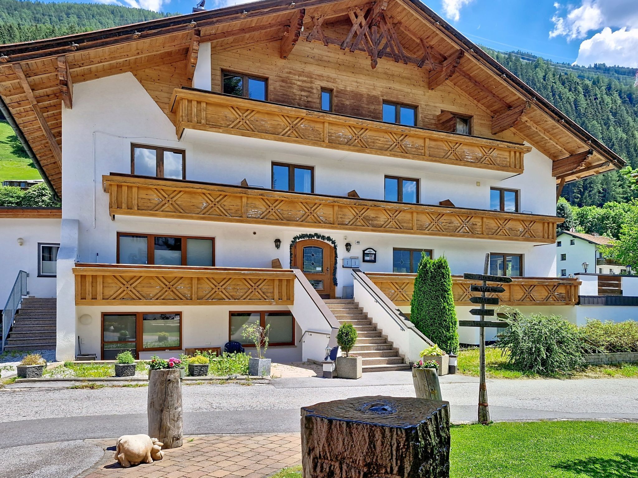 A multi-story building with a traditional Alpine architectural style, featuring wooden balconies and a staircase leading to the entrance.