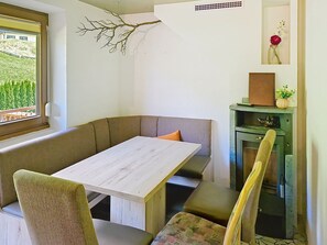 Un coin repas avec une table blanche, des bancs rembourrés et une branche décorative accrochée au mur.