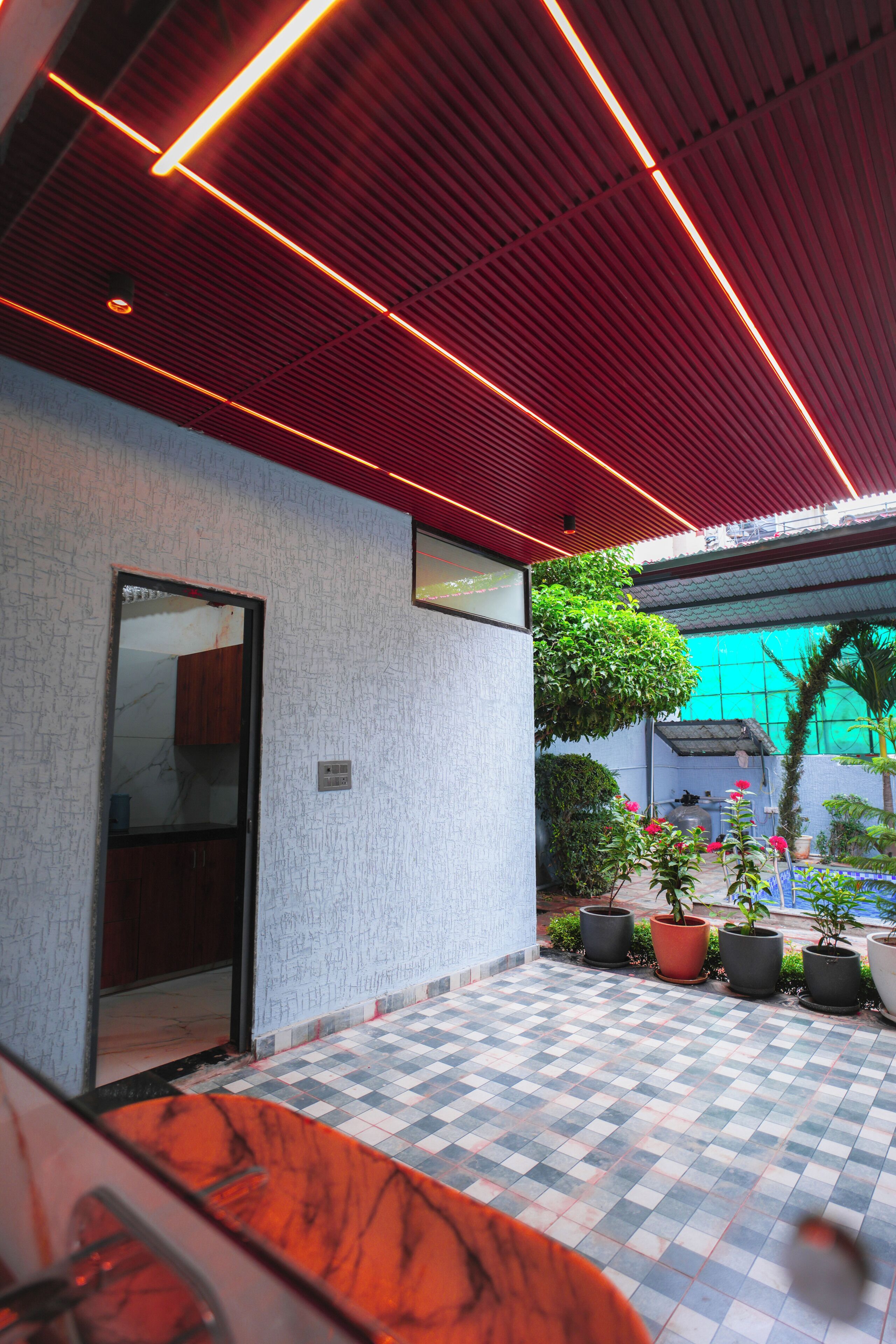 A covered outdoor area with a tiled floor, a door, and potted plants.