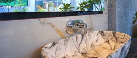 A bathroom with a marble sink, a ceiling fan, and a window with a view of greenery.