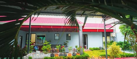 A covered outdoor area with a pool, potted plants, and a red-roofed building.