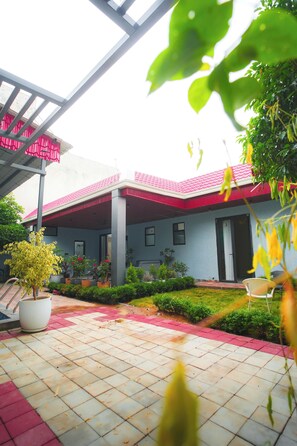 Un edificio con techo rojo y un patio cubierto. Hay macetas con plantas y un pequeño jardín al frente.