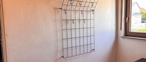 Habitación con un perchero metálico fijado a la pared, una ventana con vista a edificios y piso de baldosas.