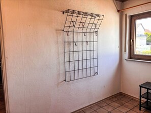 A room with a wall-mounted metal rack with hooks, a window with a view of buildings, and a tiled floor.