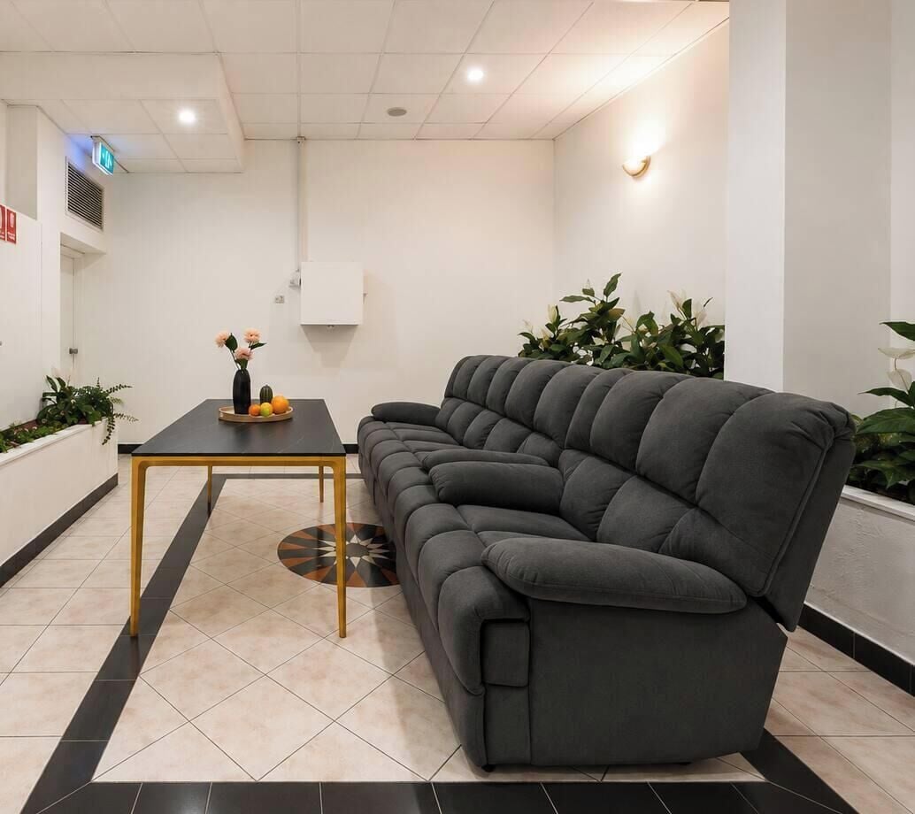 A modern living room with a dark grey sofa, a small black table with a vase of flowers, and a tiled floor with a geometric pattern.