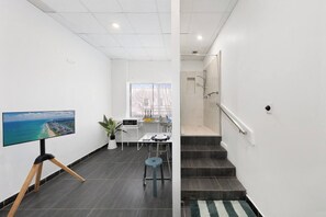 A modern interior with a flat-screen TV on a tripod, a small table with a plant, and a staircase leading to a shower area.