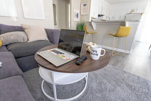 Ein modernes Wohnzimmer mit einem Laptop auf einem runden Tisch, einer Tasse und einer Fernbedienung.