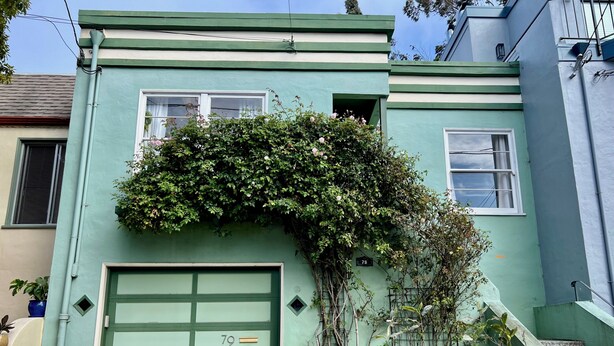 Ein Haus mit grüner Garagentür, einem Backsteinfundament und der Hausnummer 79 an der Wand.
