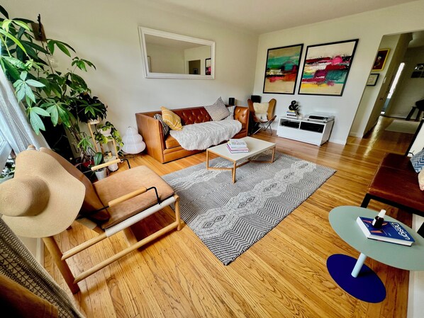 A living room with a sofa, coffee table, and a chair. There is a large mirror on the wall and a plant in the corner.