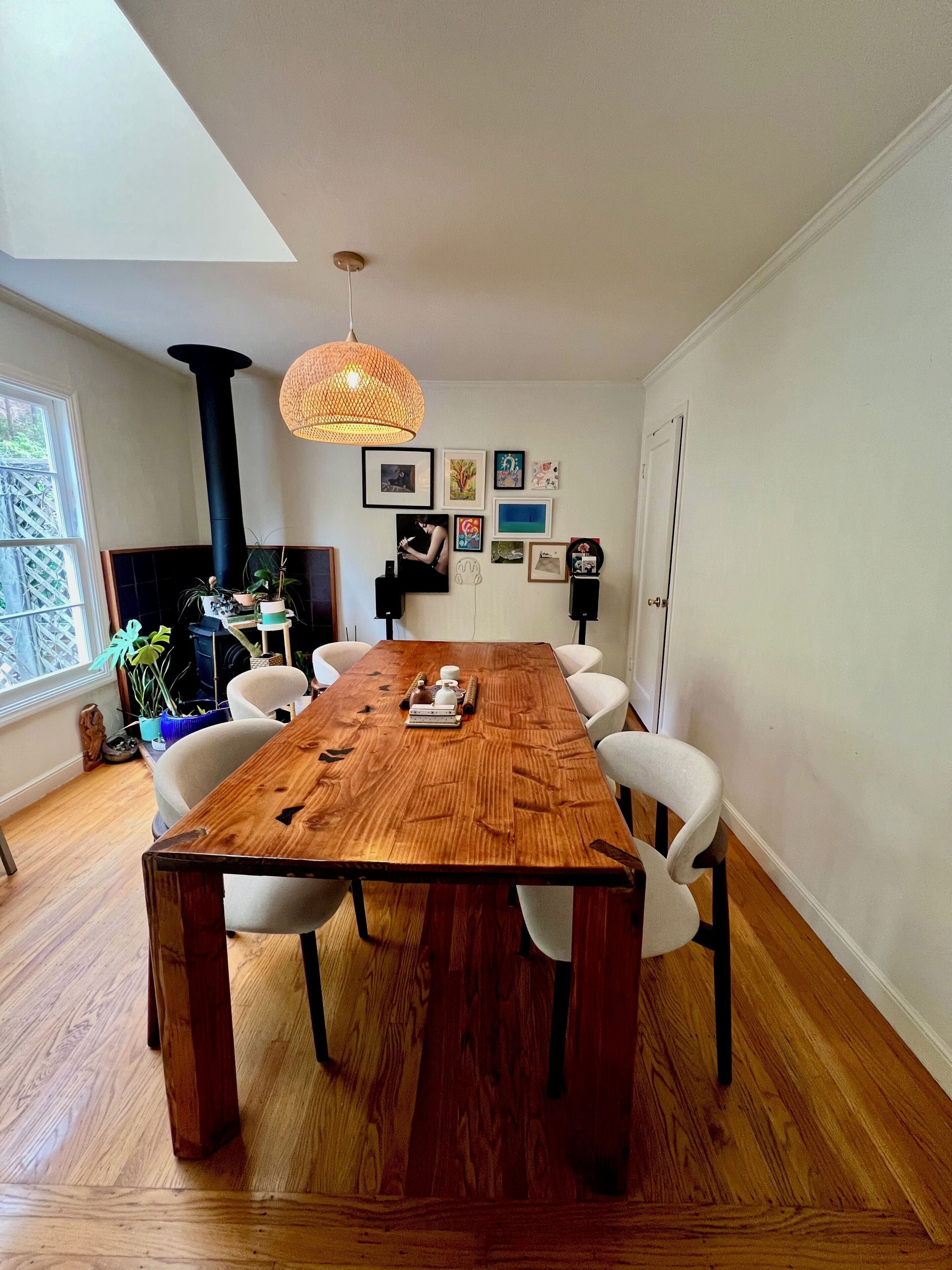 Een eetkamer met een grote houten tafel, witte stoelen, een zwarte kolom en een hanglamp.