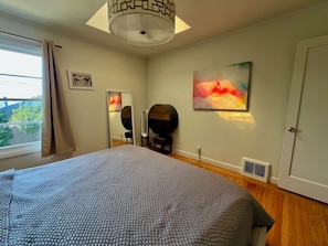 A bedroom with a bed, a window with curtains, a ceiling light fixture, a wall-mounted mirror, and a painting.