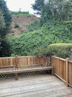 Eine Holzterrasse mit einer Bank, umgeben von dichtem Grün und einer Hanglage.