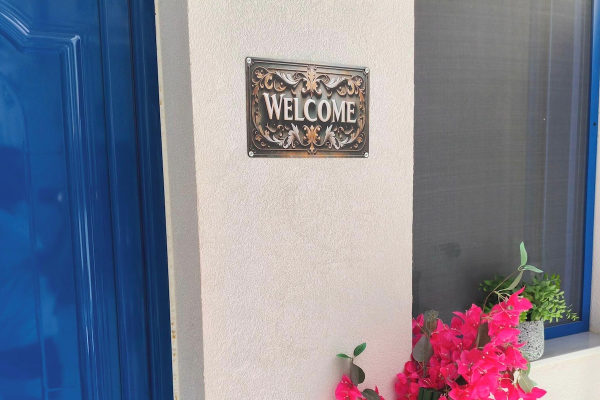 A blue door, a welcome sign, and a potted plant with pink flowers.