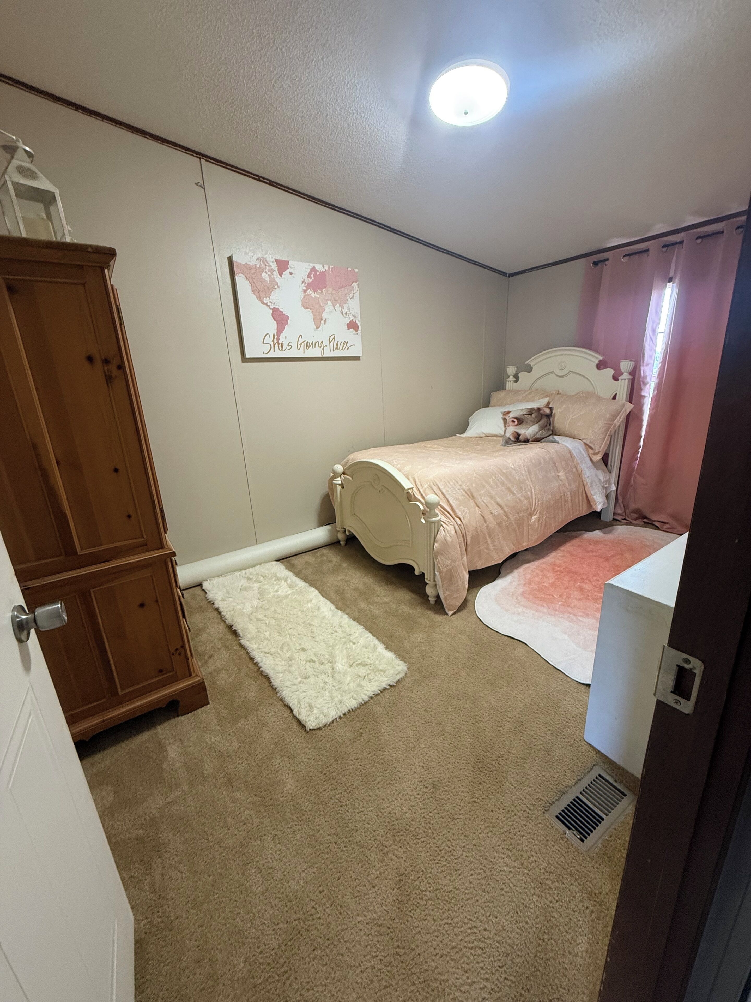 Un dormitorio con cama, armario de madera, radiador blanco, mapa mundial y puerta blanca.