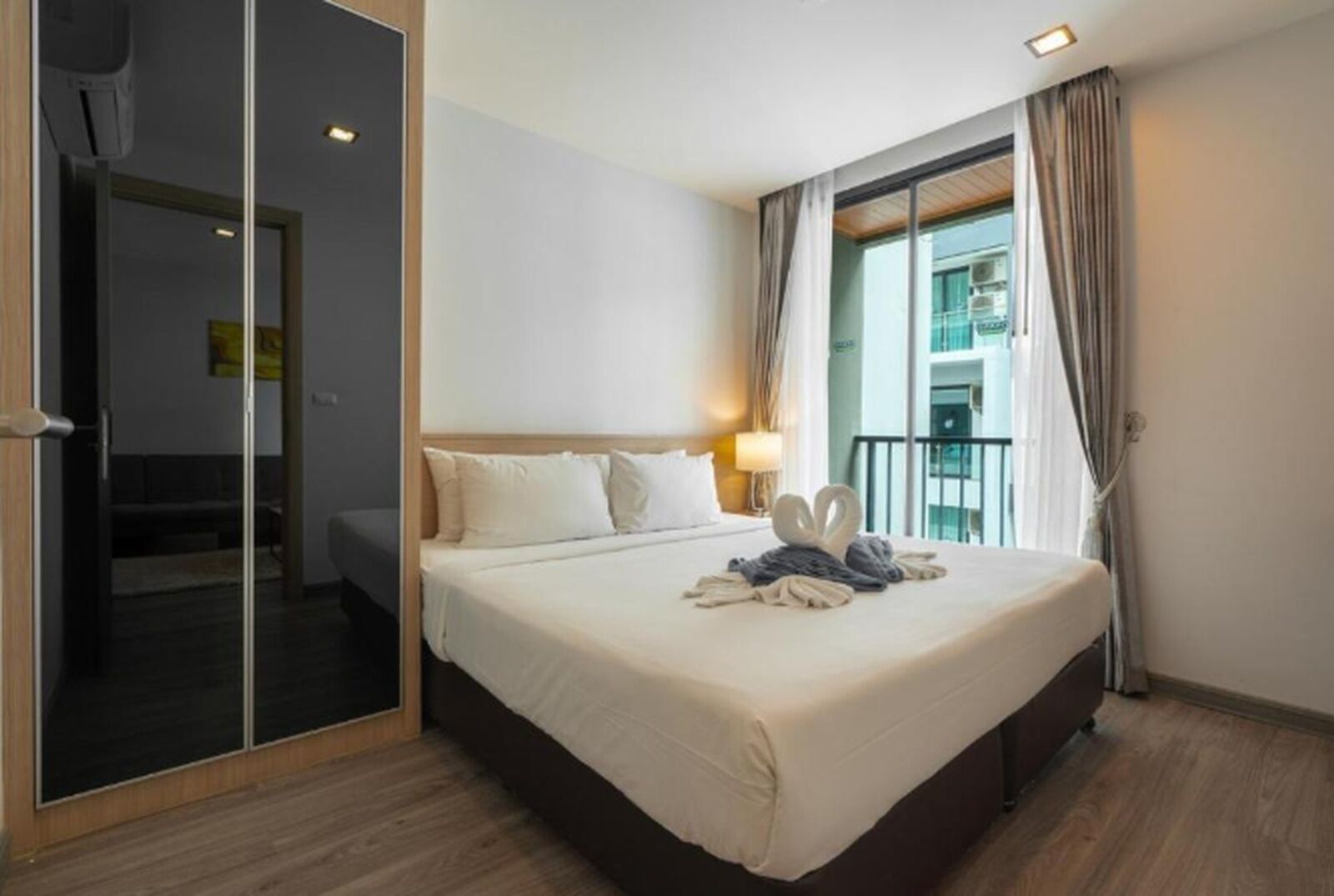 A hotel room with a bed, a bedside table, a lamp, a window with curtains, and a view of the outside.