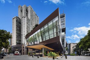 A modern hotel with a prominent entrance, large windows, and a parking area.