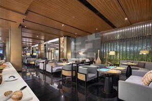 A modern hotel lobby with a long reception desk, seating areas, and a large window with a view.