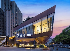 Un moderno edificio de hotel con un llamativo letrero 'HAIYI HOTEL', amplias ventanas y un estacionamiento.