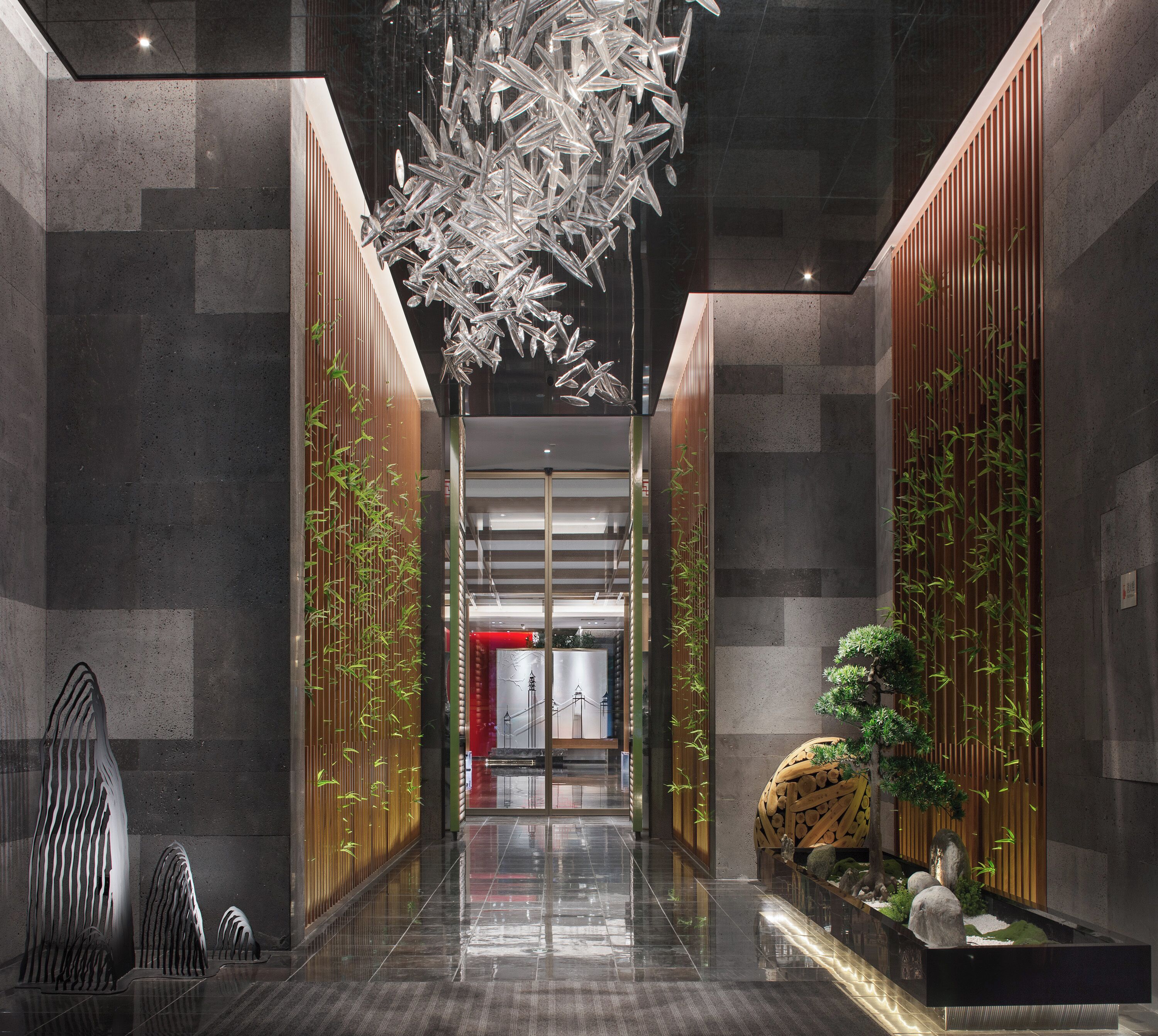 A modern lobby with a reflective floor, vertical bamboo panels, and a hanging metallic sculpture.