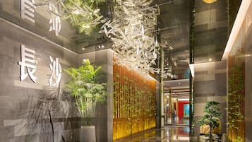 Een moderne lobby met een waarschuwingsbord voor een natte vloer, een receptiebalie en een decoratieve wand met hangende elementen.