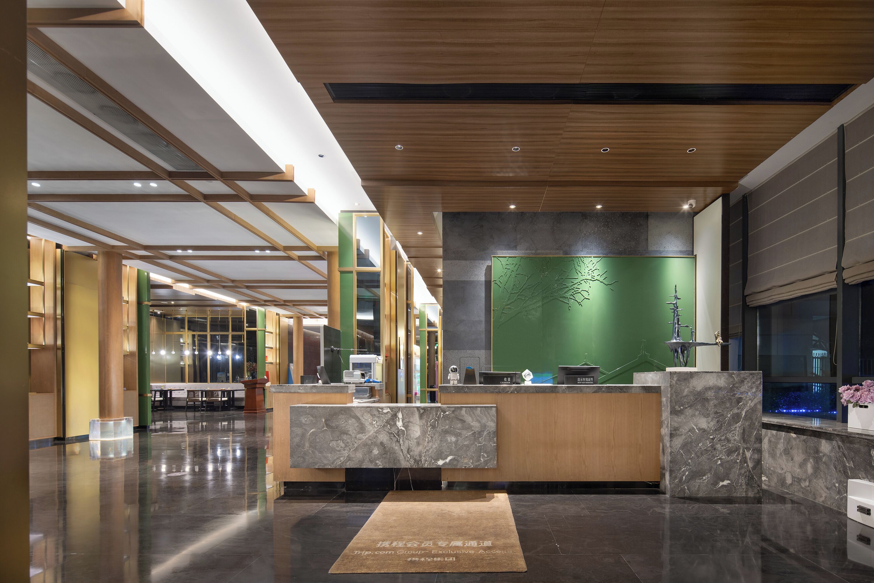 Un área de recepción moderna con un mostrador de mármol, una pared verde con un relieve de árbol y un techo de madera.