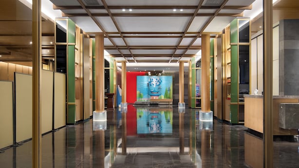 Un hall d’hôtel doté d’un sol réfléchissant, d’un comptoir d’accueil central et d’une fresque colorée sur le mur.